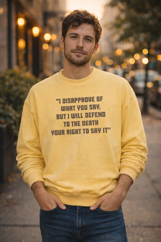 Millennial man wearing a yellow Freedom of Speech sweatshirt standing on a softly lit city street at dusk.