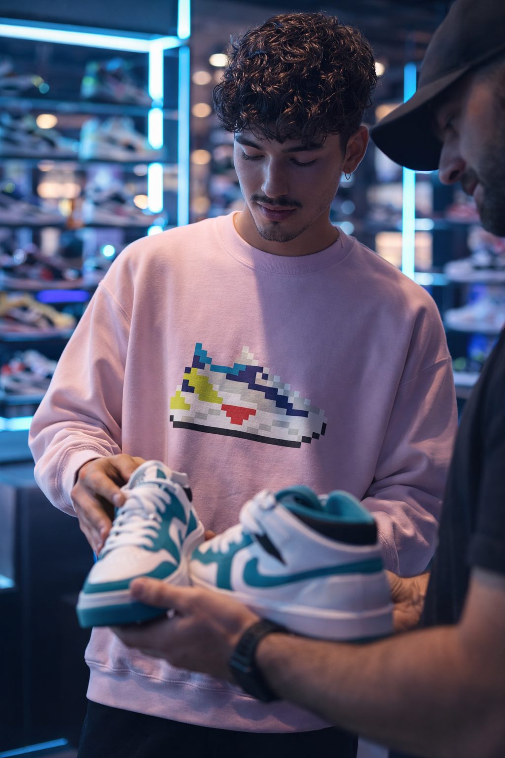 Young man in sneaker store wearing 8-bit sneaker sweatshirt, holding shoes with pixel sneaker graphic