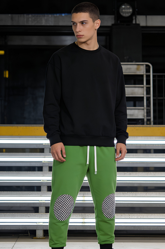 Model wearing green joggers with gray checkered knee patches standing in an urban setting, casual streetwear outfit