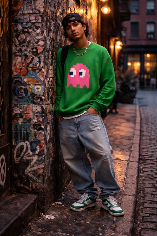 Young male wearing a green sweater with a pink pixelated ghost design, standing against a graffiti-covered wall.