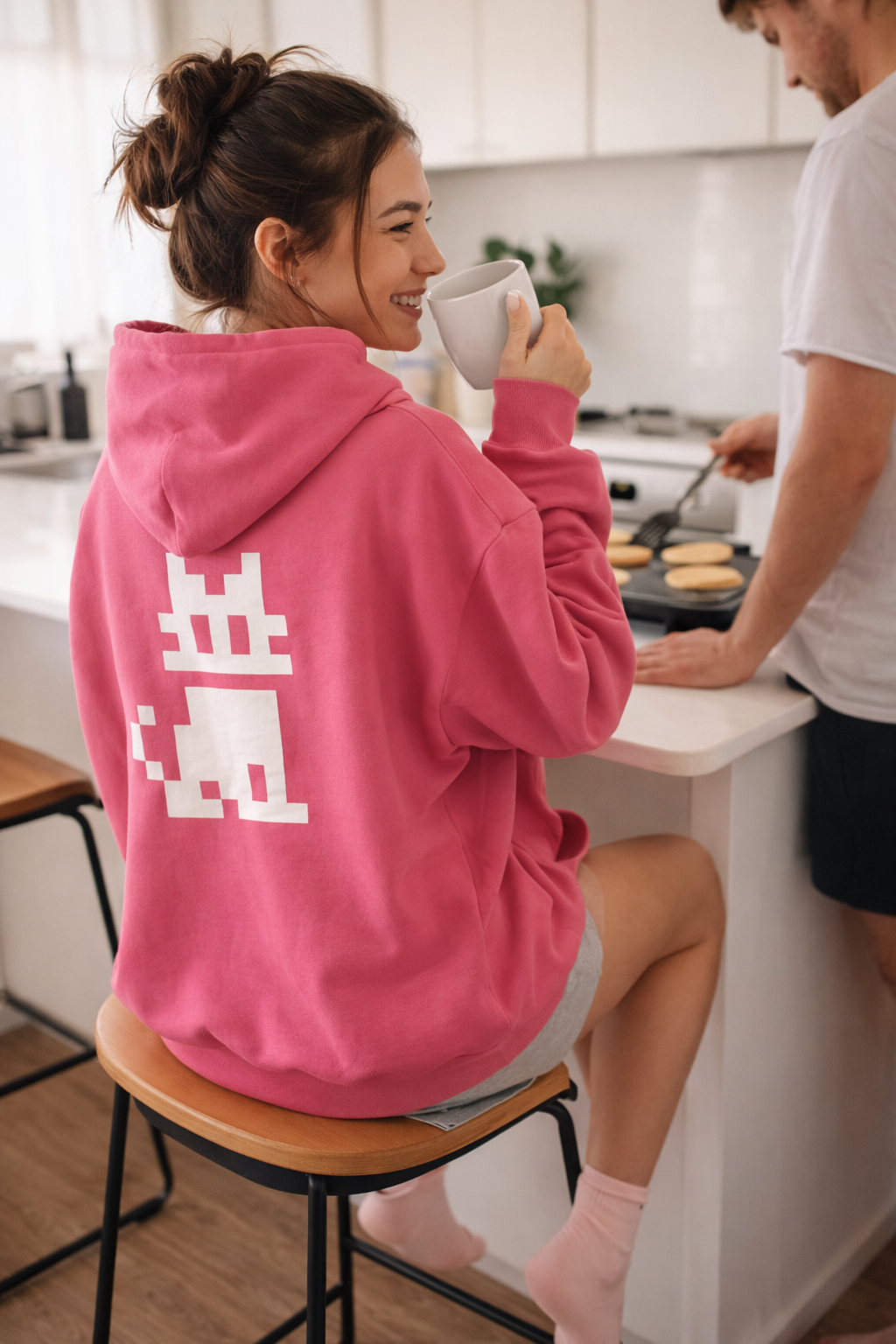 Woman wearing a pink Pixel Cat Unisex Hoodie  in a kitchen setting