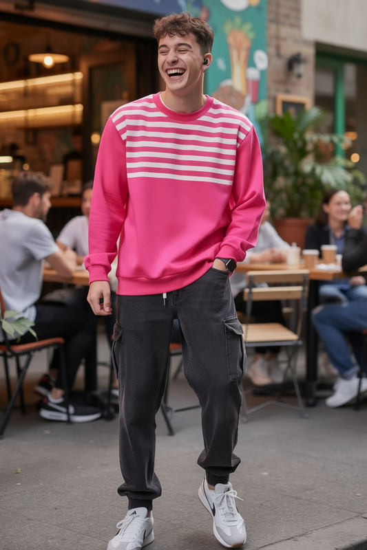 Man wearing the Pink Striped Sweatshirt and dark pants standing on a street with people and shops in the background.