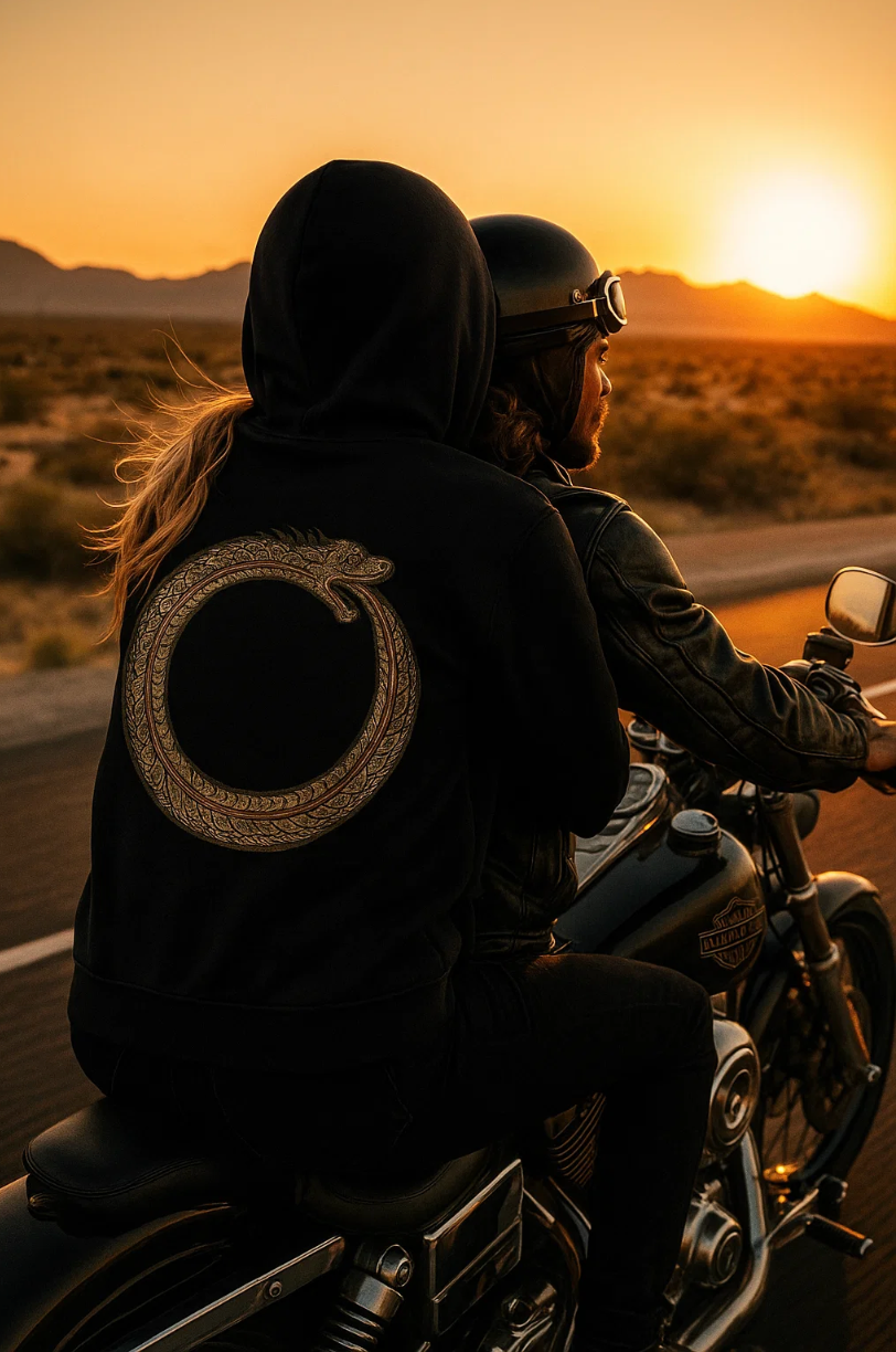 Two people riding a motorcycle on a desert road at sunset.