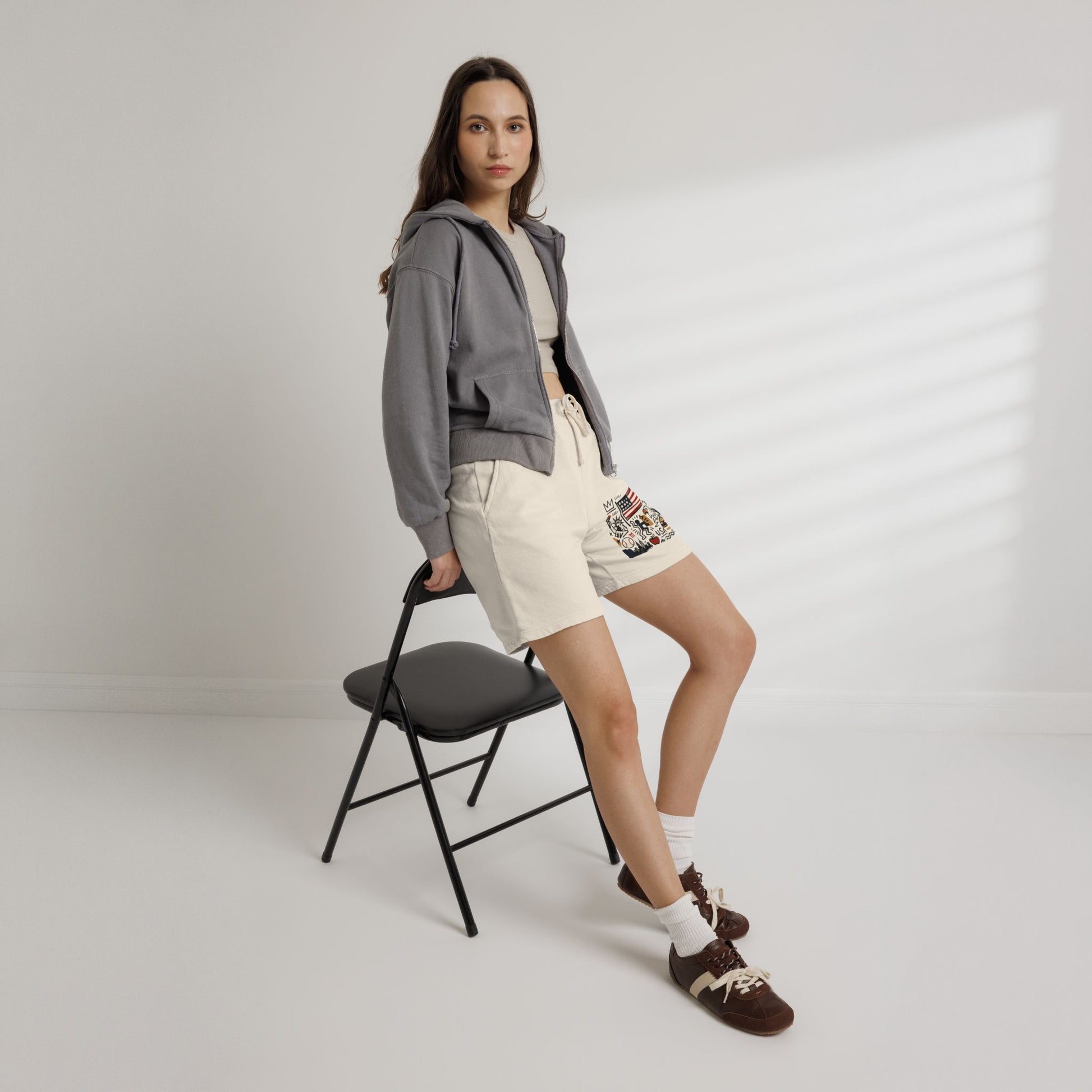 Female model wearing cream America flag sweat shorts seated studio mockup