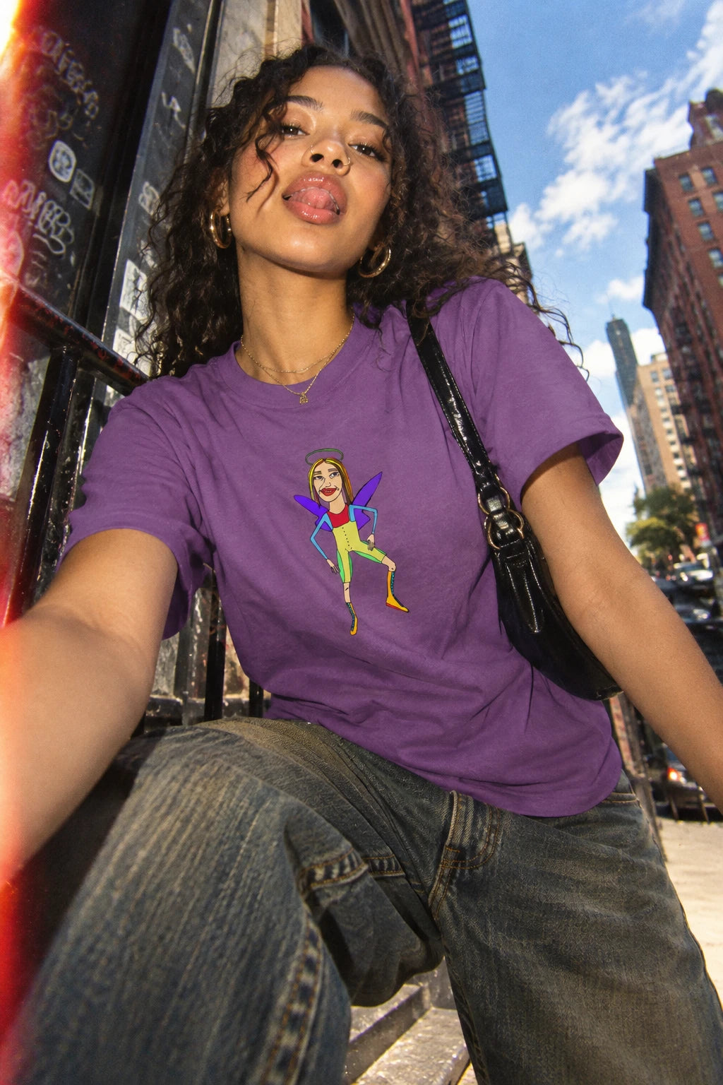 Millennial man wearing the Angelic Sportsy graphic T-shirt in purple in an urban street setting