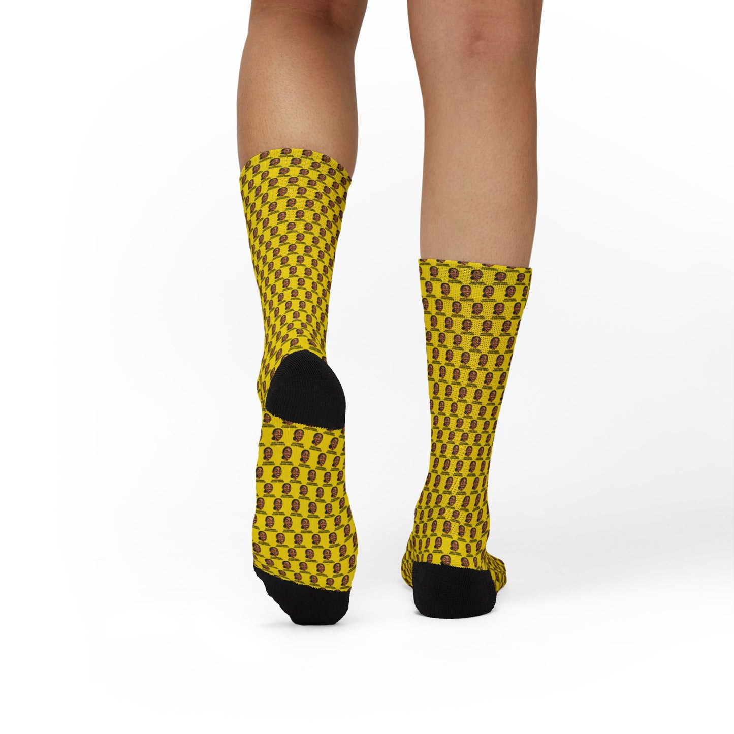 Rear view of yellow AOC crew socks featuring repeating Alexandria Ocasio-Cortez artwork pattern worn by a model.