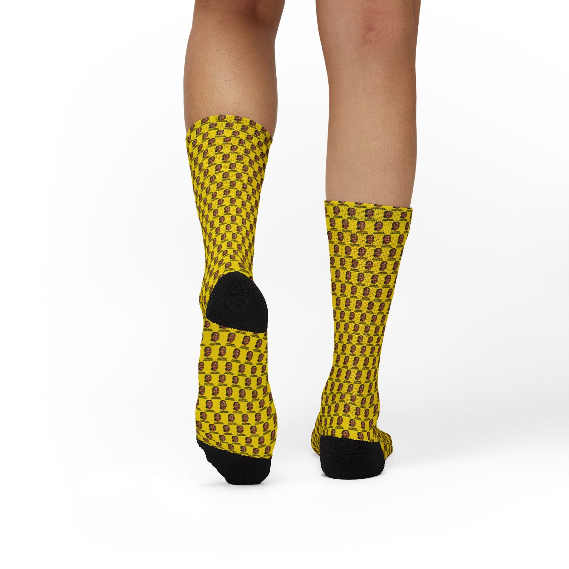 Rear view of yellow AOC crew socks featuring repeating Alexandria Ocasio-Cortez artwork pattern worn by a model.