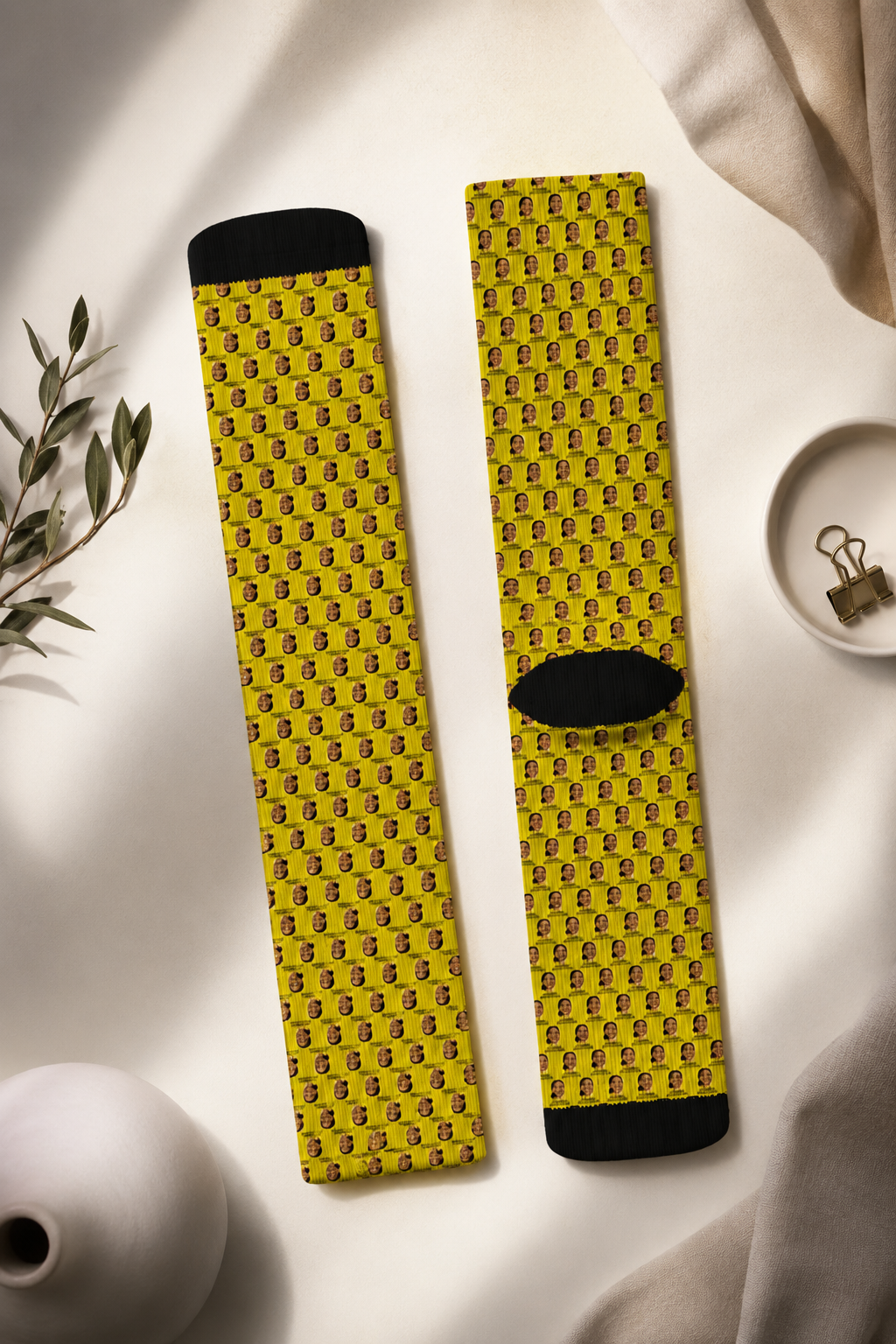 Flat-lay editorial photography of yellow AOC crew socks featuring repeating Alexandria Ocasio-Cortez artwork on a soft neutral fabric background.