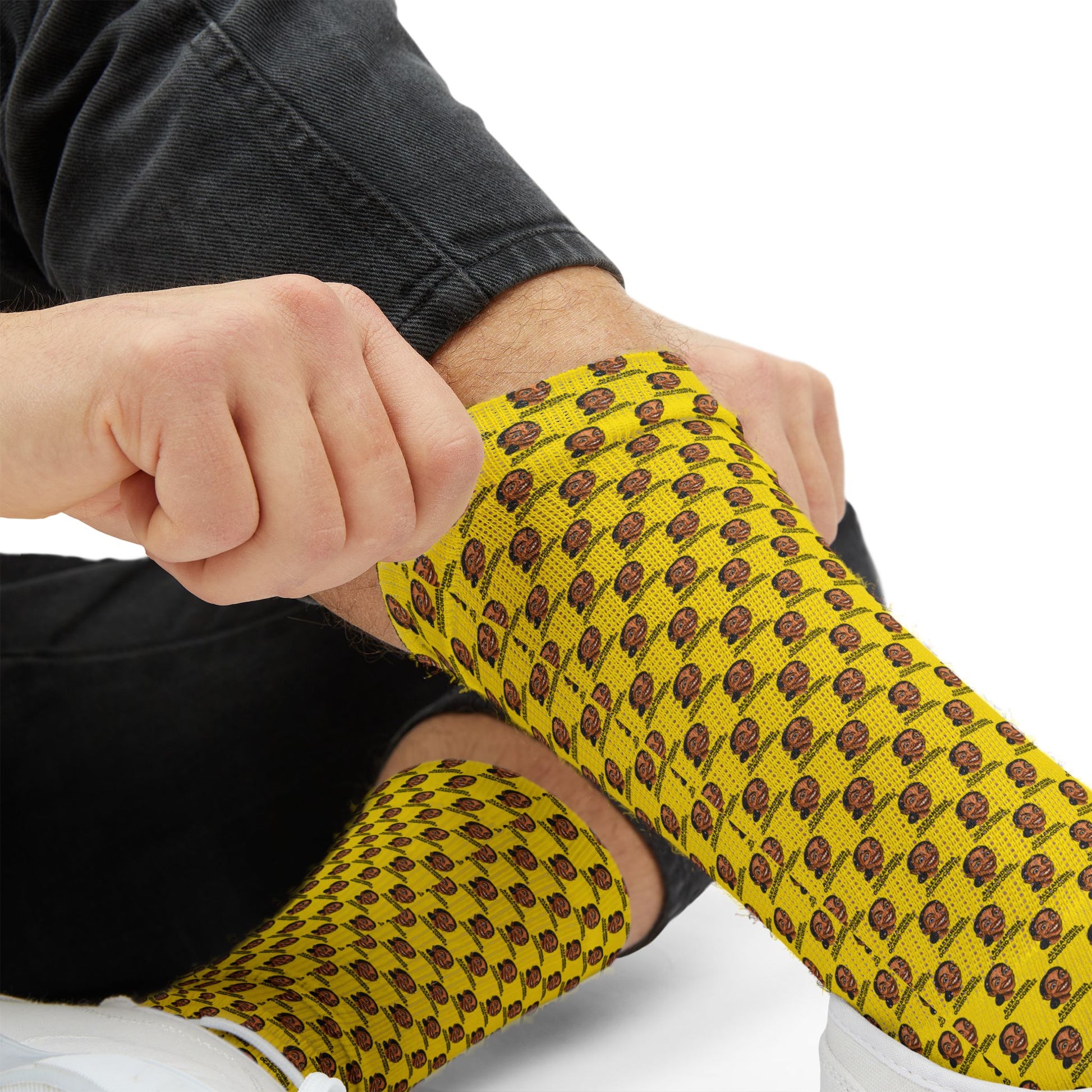 Close-up detail of yellow AOC crew socks showing stretch fabric construction and repeating Alexandria Ocasio-Cortez artwork pattern.
