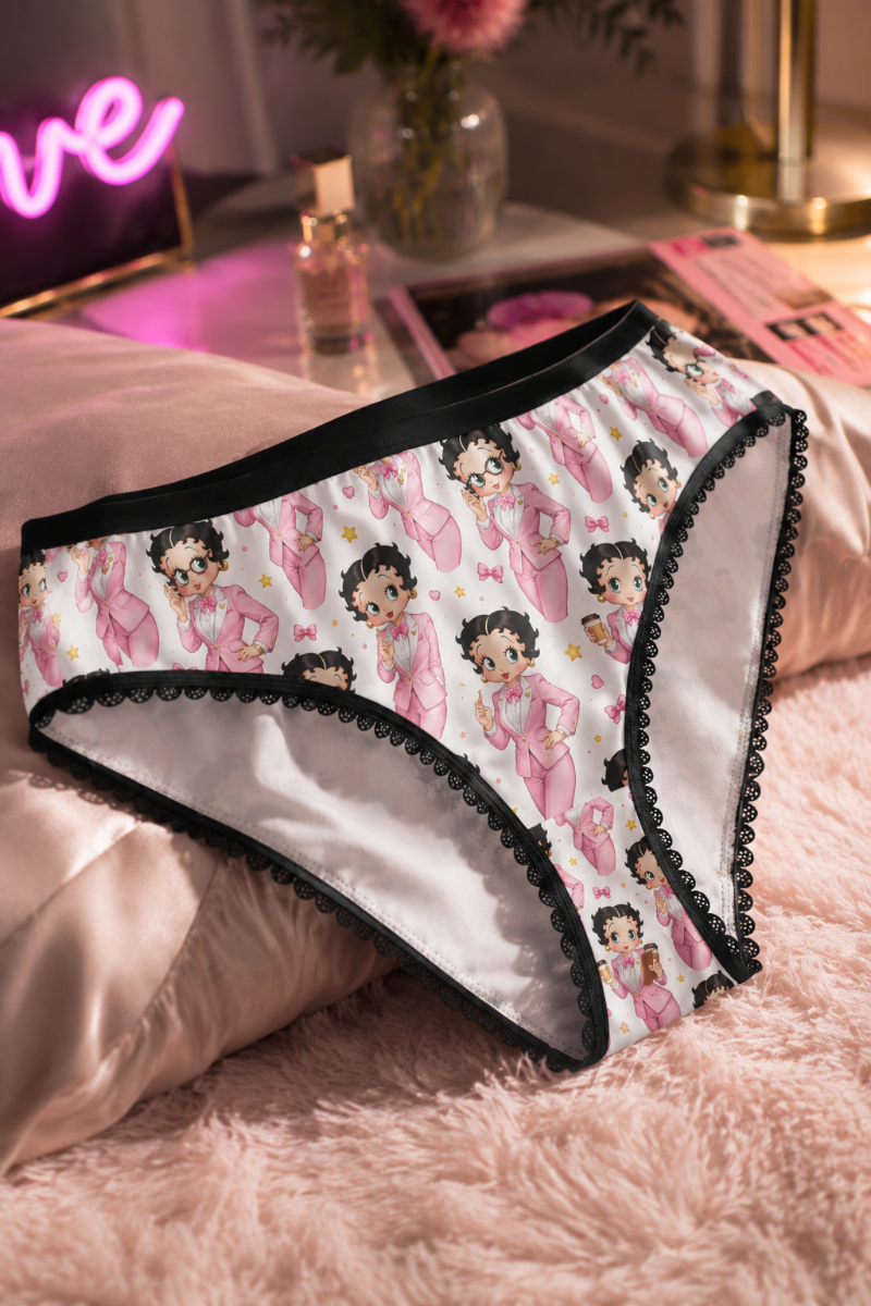 Betty Boop pink print women’s panties with black lace trim styled in a soft pink bedroom flat lay