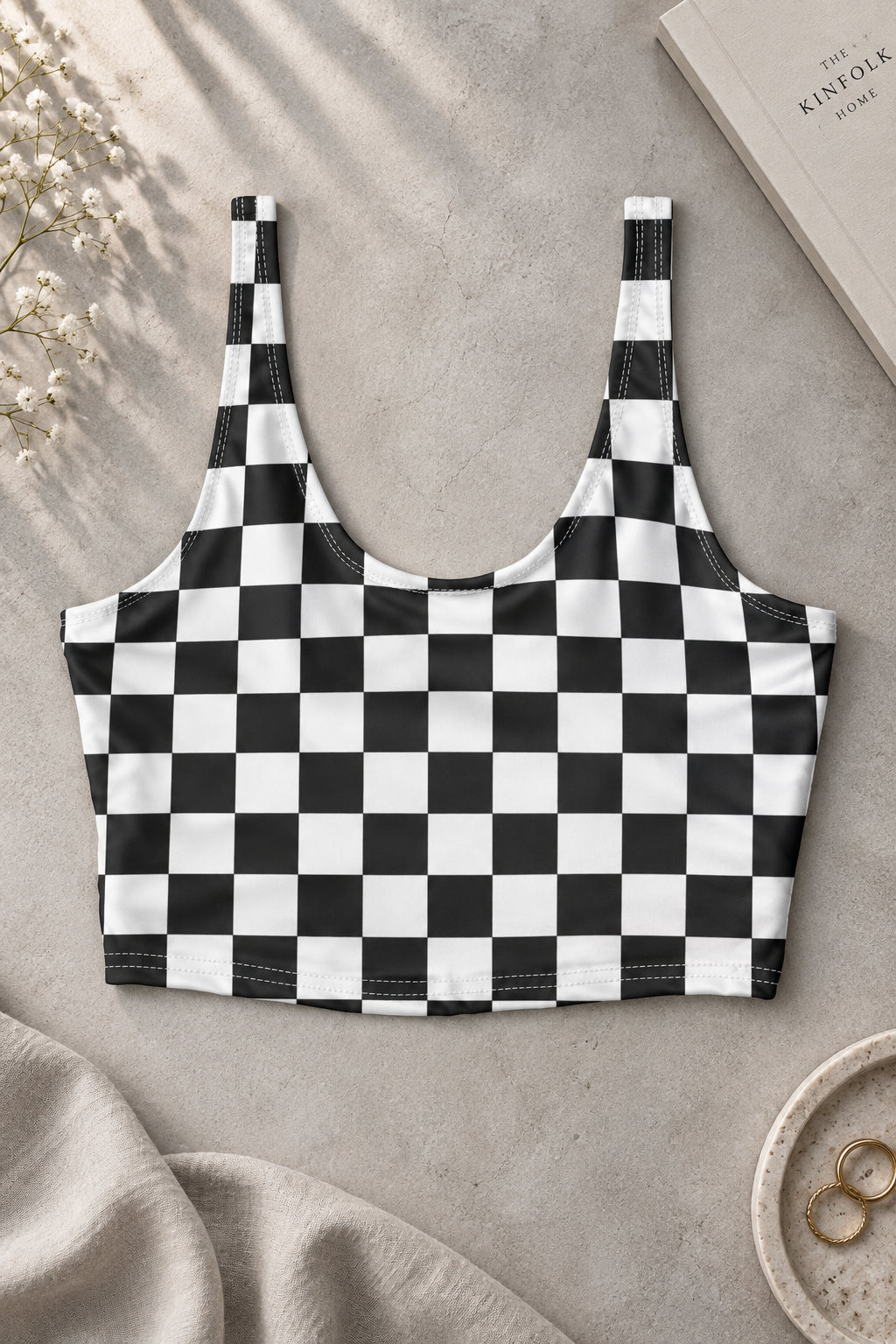Front view of black and white checkerboard sports bra with a scoop neckline and cropped athletic fit, photographed on a warm beige background.