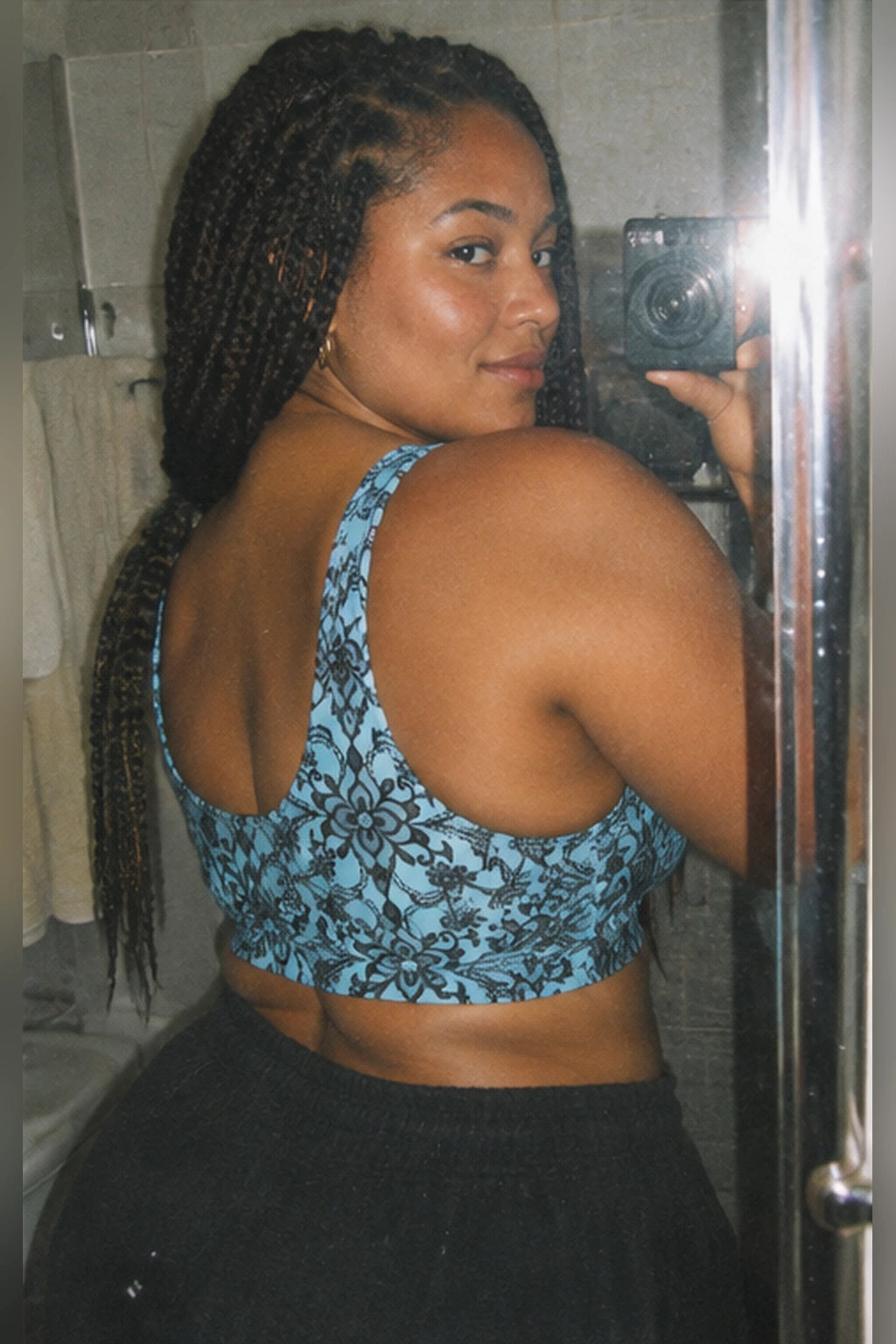 Woman wearing a blue floral lace print sports bra with black sweatpants, showing its U-shaped back and wide straps in a mirror selfie.