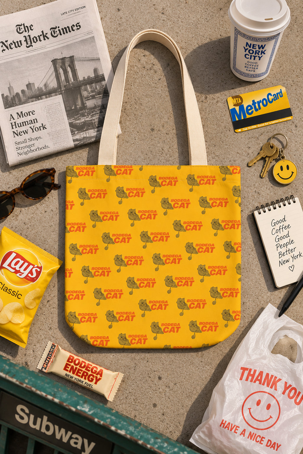 Bodega Cat yellow 16 x 16 tote bag flat lay with New York City accessories