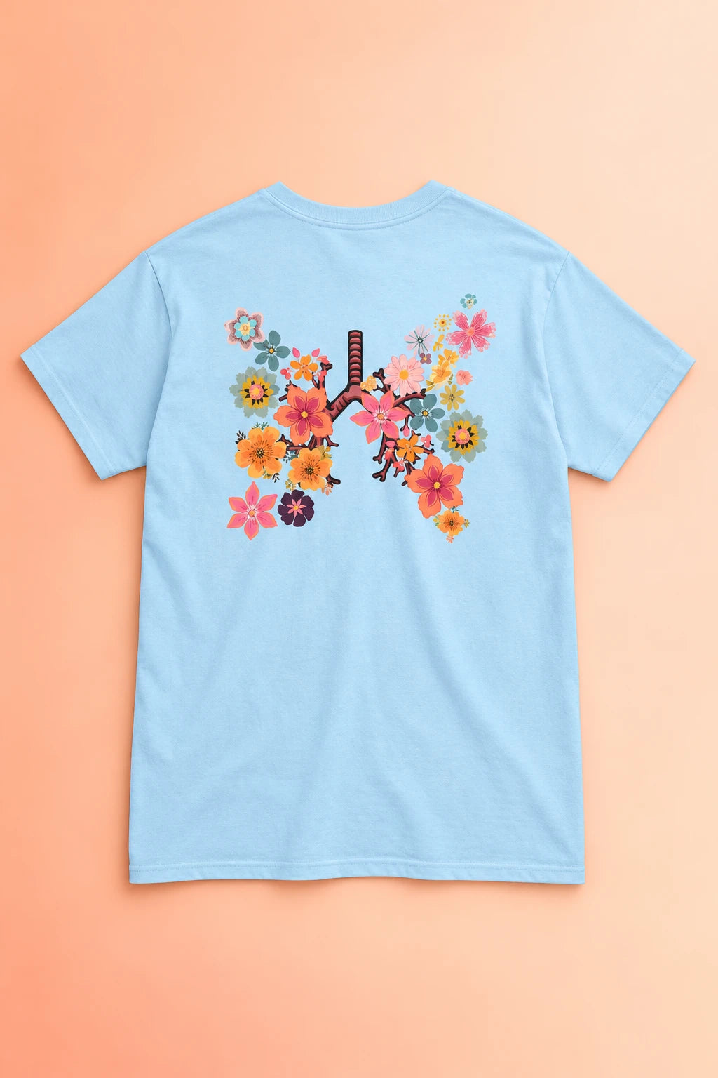 Light blue Breath T-shirt laid back-side up on a peach gradient, showing the colorful floral lungs graphic.