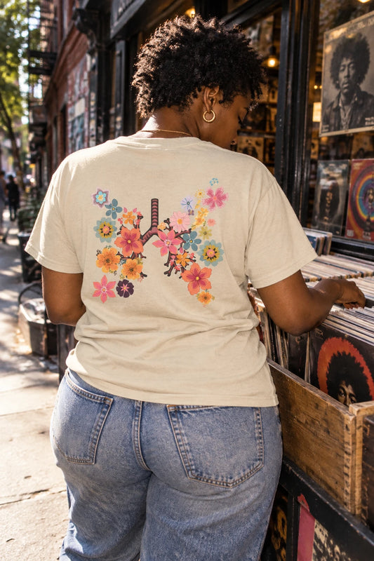 Woman browsing vinyl records in a sand Breath T-shirt with the floral lungs graphic visible on her back.