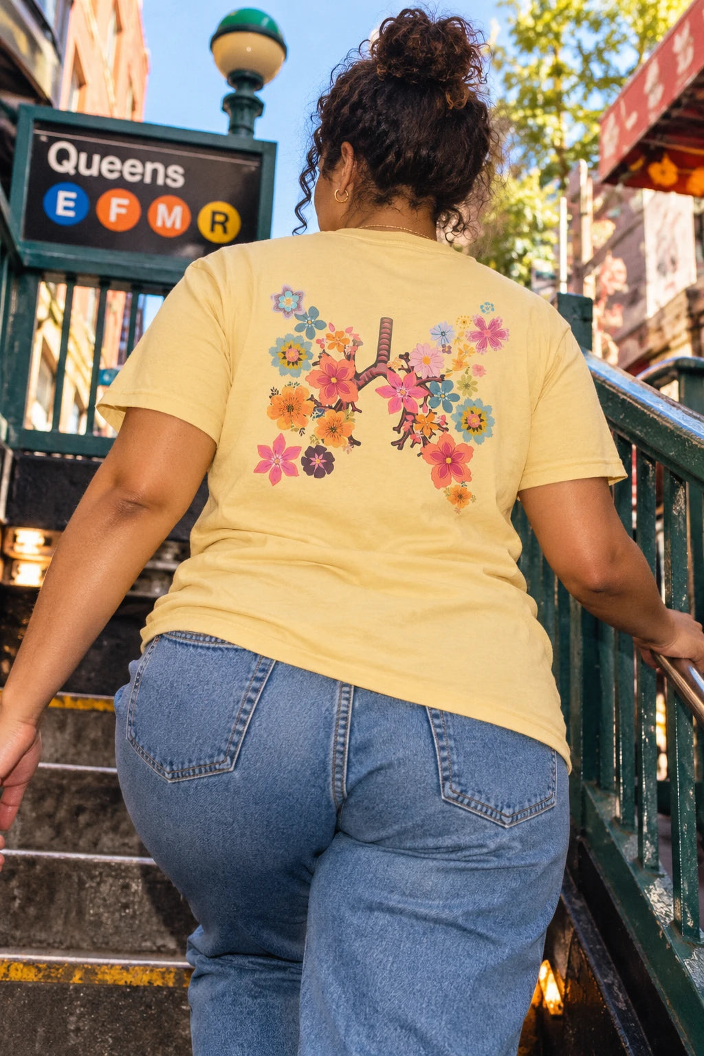 Woman climbing subway steps in a yellow Breath T-shirt with a colorful floral lungs graphic on the back.