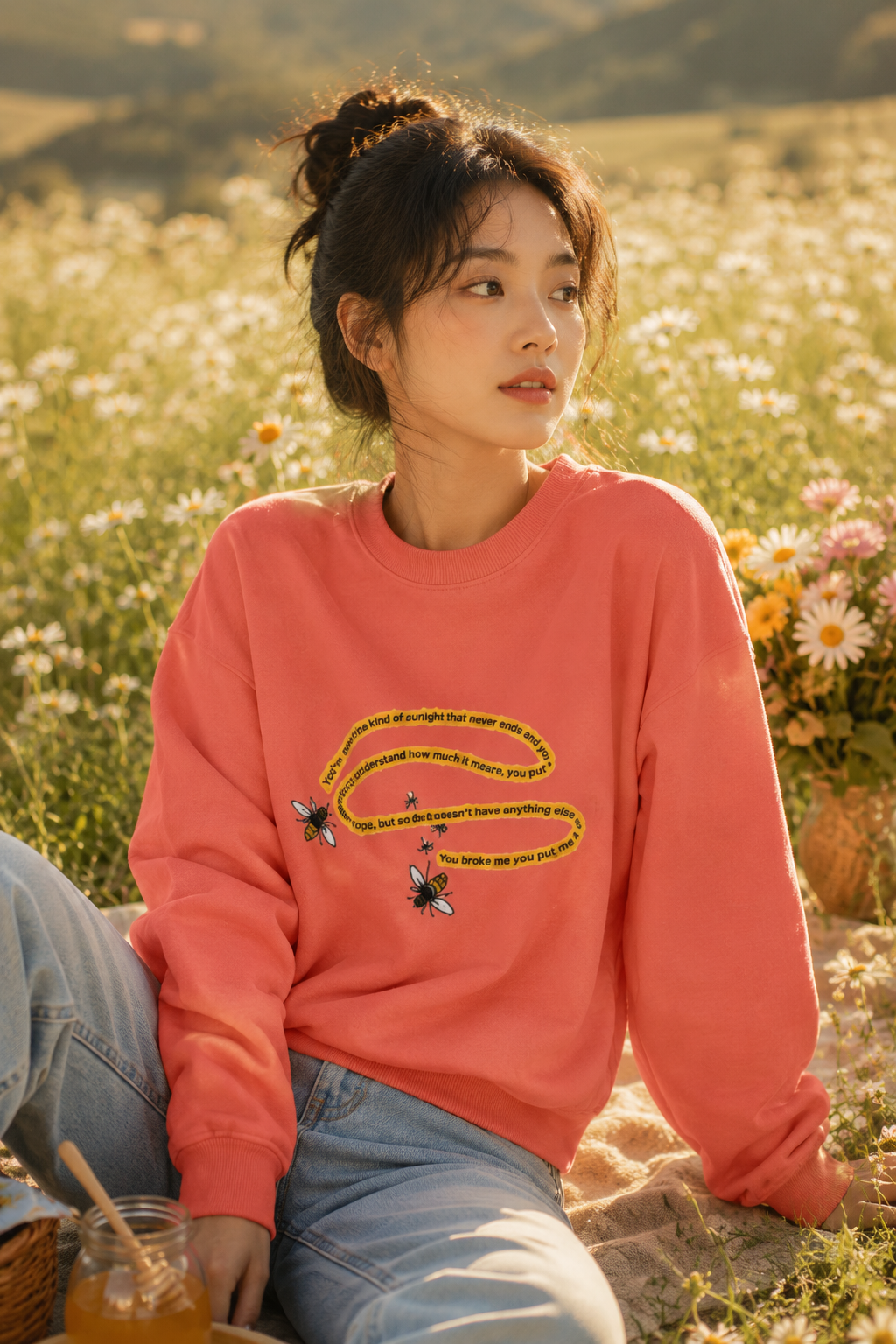 Woman wearing a coral bumblebee sweatshirt in a warm sunlit field of daisies.