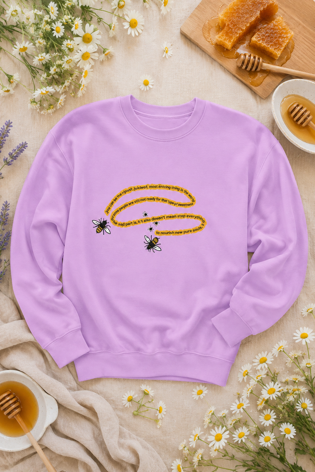 Lavender bumblebee sweatshirt styled with daisies, honeycomb and honey in an editorial flat lay.
