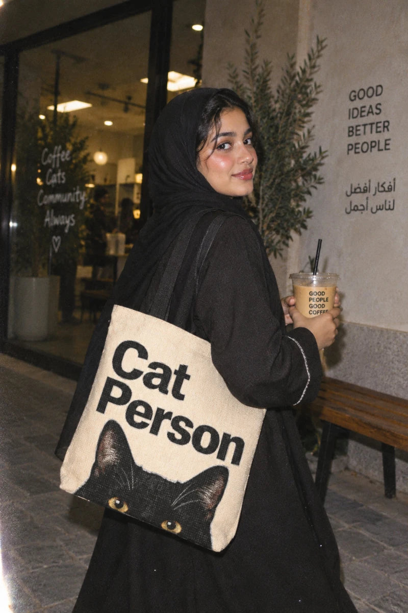 Saudi Gen Z woman carrying the Cat Person black cat tote bag outside a café