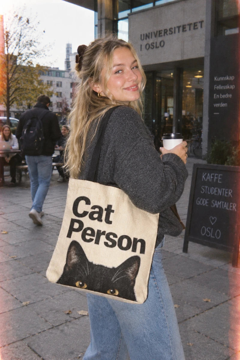 Swedish Gen Z student in Oslo carrying the Cat Person black cat tote bag in a college scene with a disposable camera aesthetic