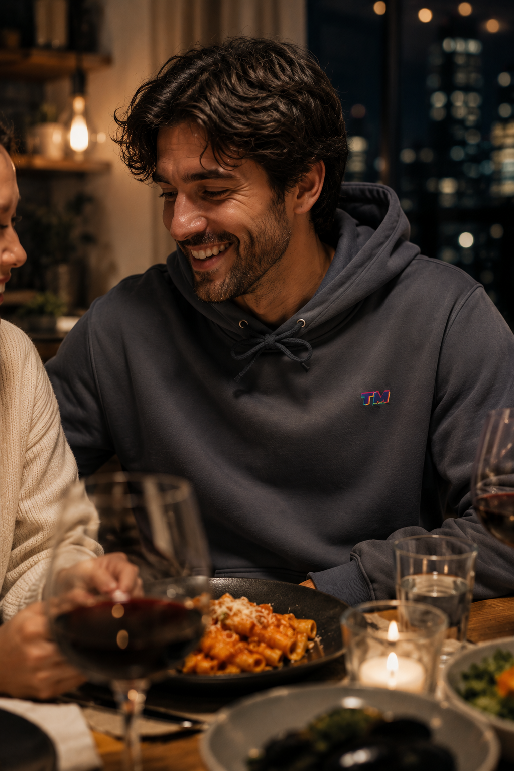Male millennial wearing the Tantrum Media EcoSmart charcoal hoodie during a cozy dinner in a Brooklyn Heights townhouse.