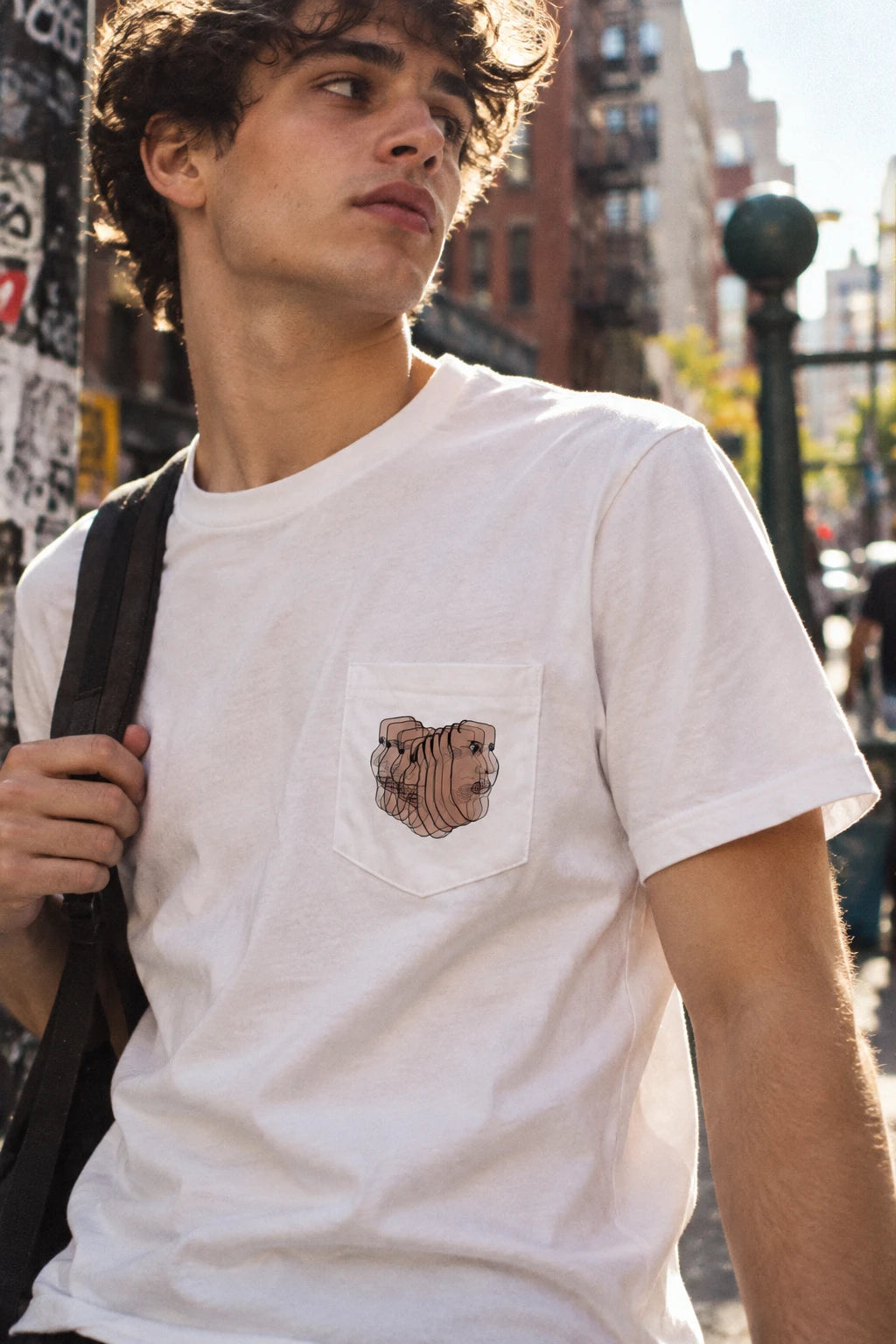 Young man wearing the Charlie Deluxe abstract face pocket T-shirt in white in an urban street setting