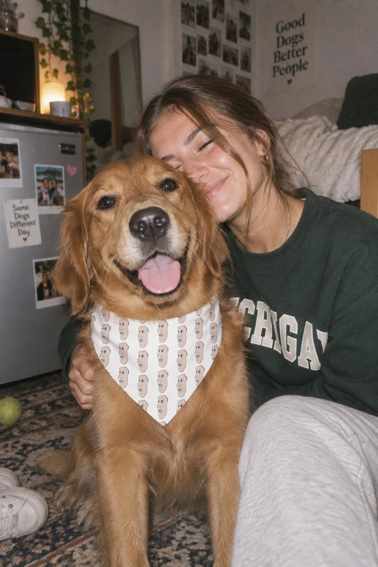 Golden retriever wearing the Charlie pet bandana with repeating hand-drawn face print beside a young pet parent