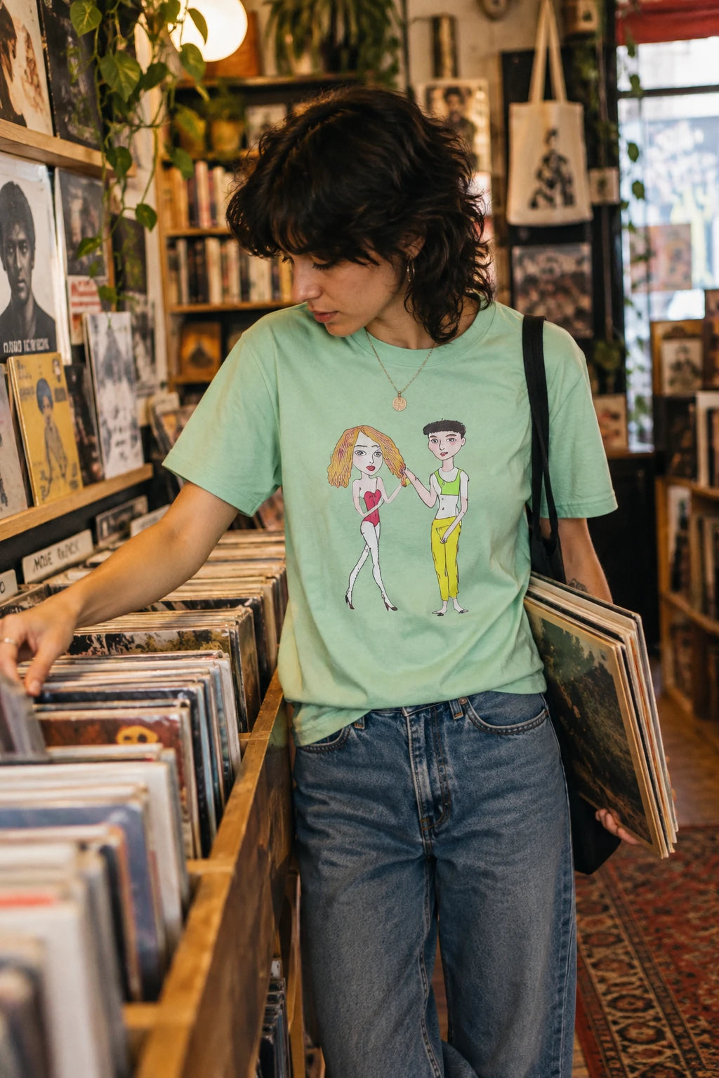 Person wearing mint Charlotte & Van graphic T-shirt while browsing a record store