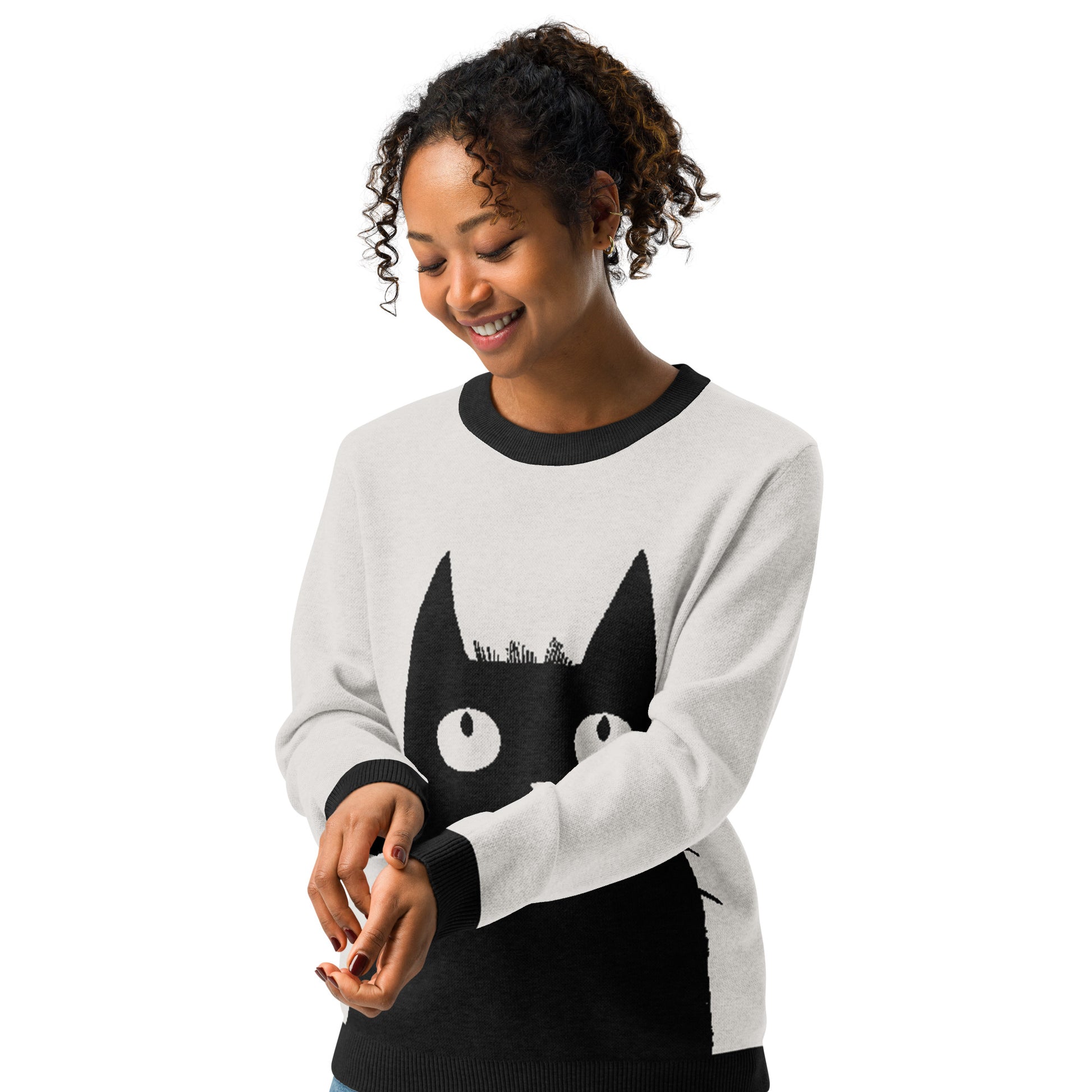 Studio image of a person wearing the cat graphic sweater smiling and holding the sleeve.
