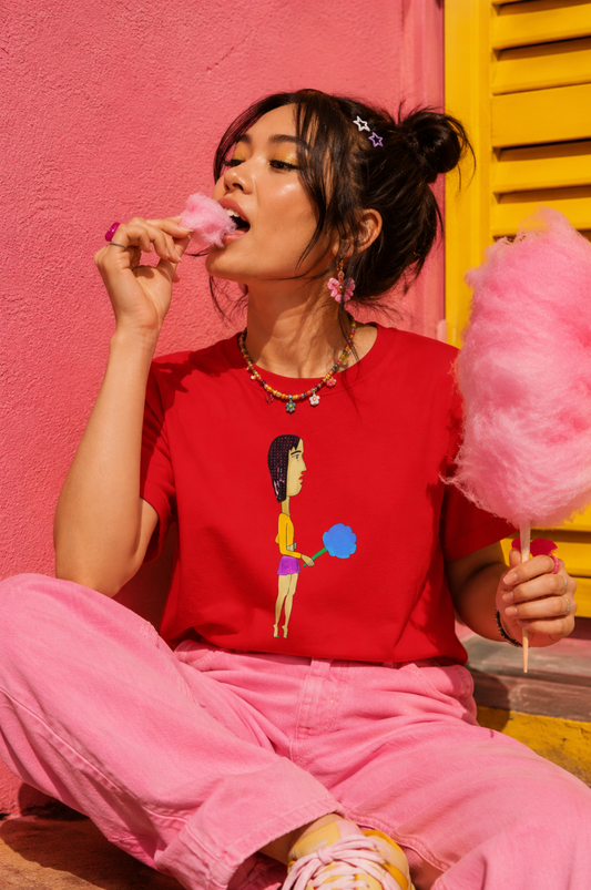 Young woman wearing the Cotton Candy Graphic Unisex T-Shirt while enjoying cotton candy in a colorful carnival-inspired editorial setting.