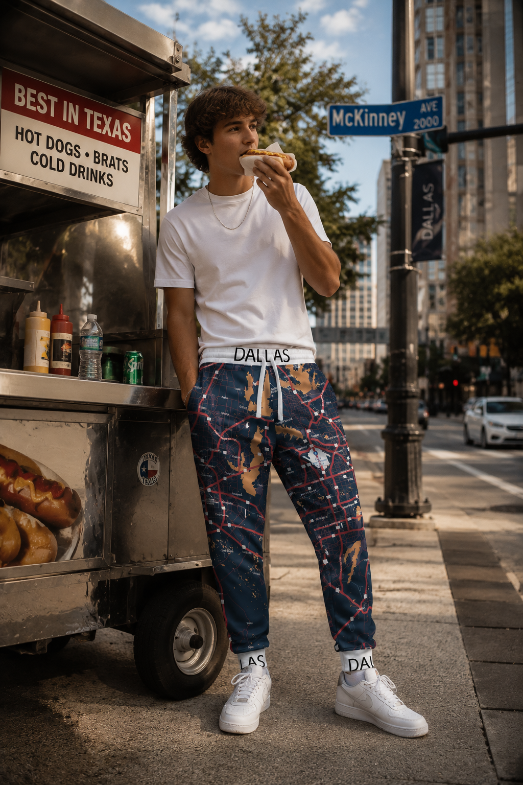 Male Gen Z wearing Dallas Map Joggers while eating a hot dog from a downtown Dallas street vendor in a cinematic editorial scene.