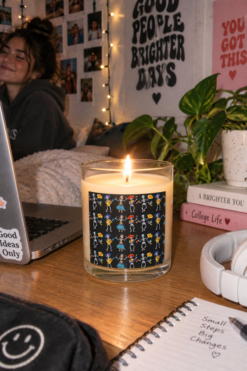 Lit Dancing Skeletons candle on a cozy desk with plants, notebook and warm indoor decor