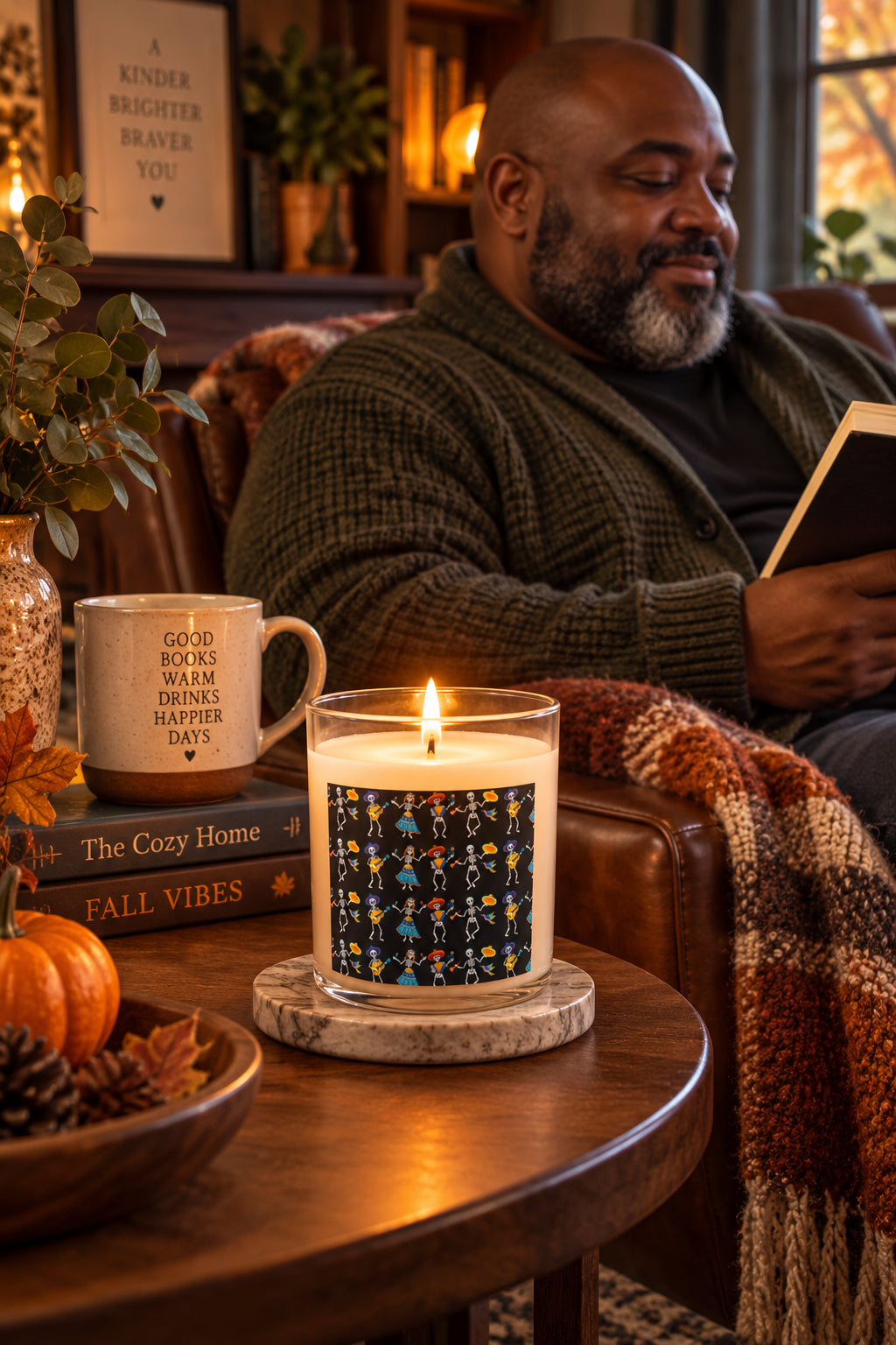 Lit Dancing Skeletons candle on a side table beside a man reading in a cozy autumn living room