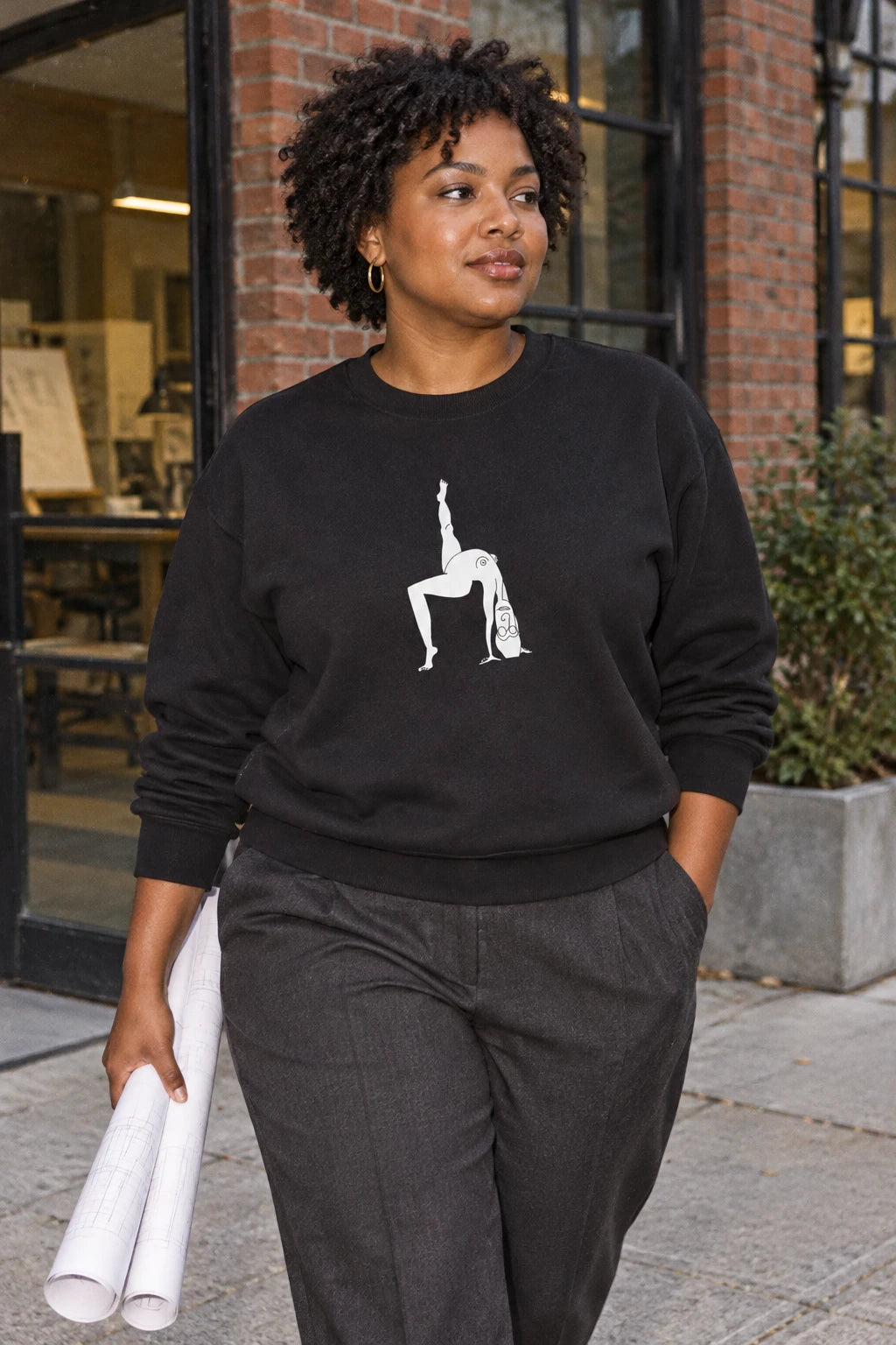 Woman wearing the black Elastika Girl unisex graphic crewneck sweatshirt with original white line art on a city sidewalk.