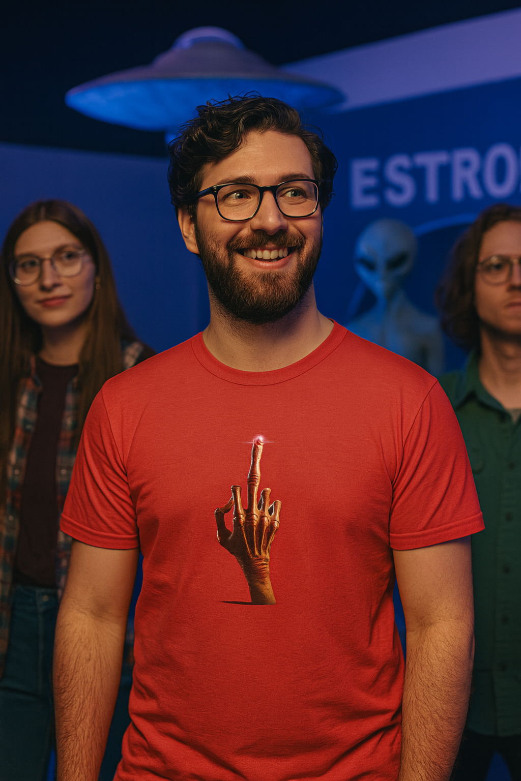 Man wearing a red alien middle finger graphic T-shirt at an indoor event with a UFO display.