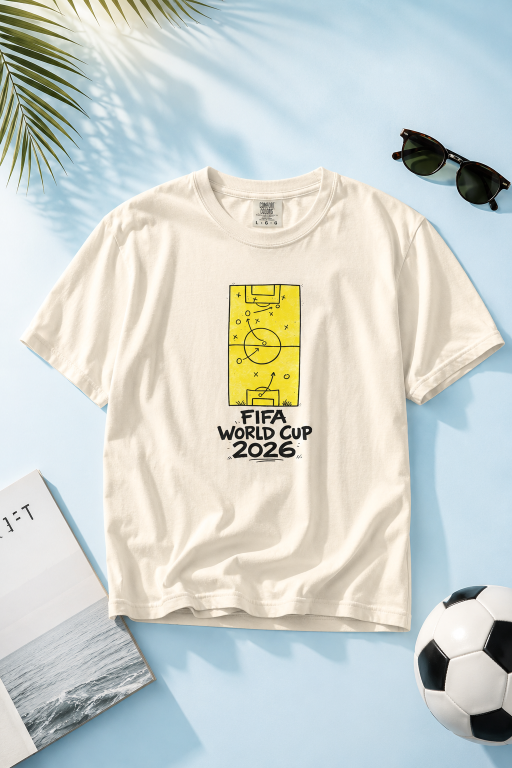 FIFA World Cup 2026 Fan Tee flat-lay photography featuring soccer tactics graphic on a soft pastel blue background with soccer-inspired lifestyle props
