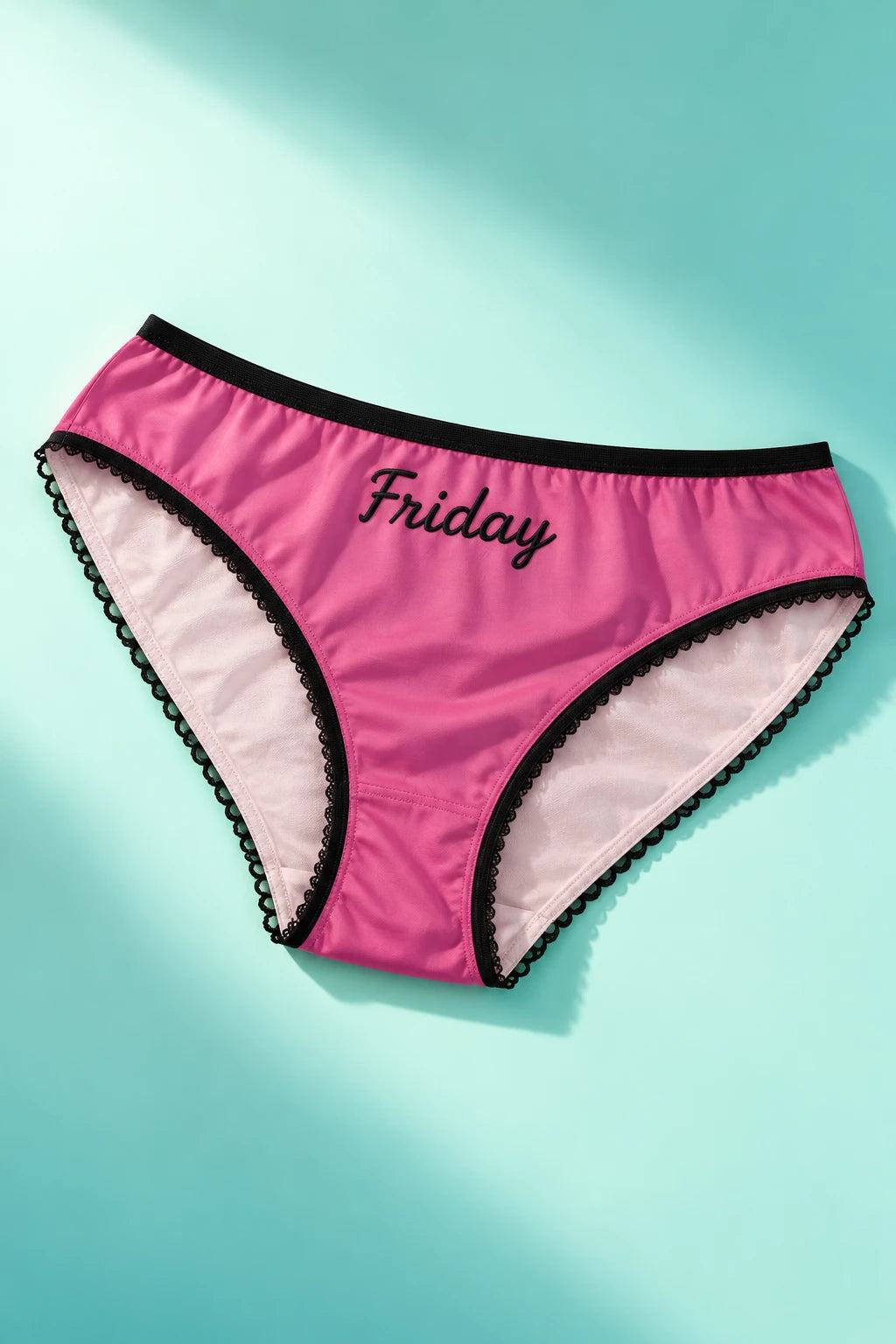 Tantrum Media Friday Panty in pink with black Friday script and scalloped trim, laid flat on a mint and aqua gradient background.