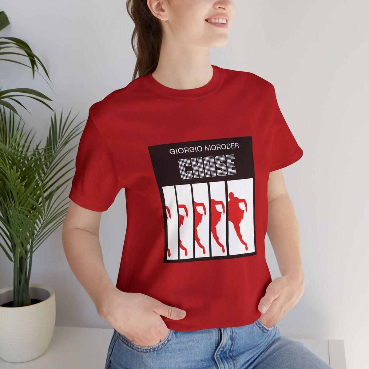 Woman wearing a red Giorgio Moroder Chase graphic T-shirt with blue jeans, showing the front cover-art print.