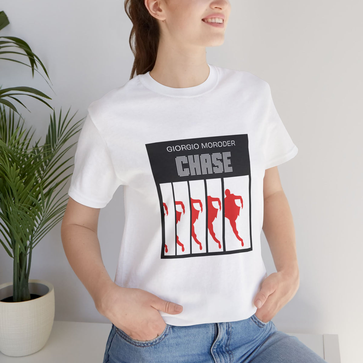 Woman wearing a white Giorgio Moroder Chase graphic T-shirt tucked into blue jeans.