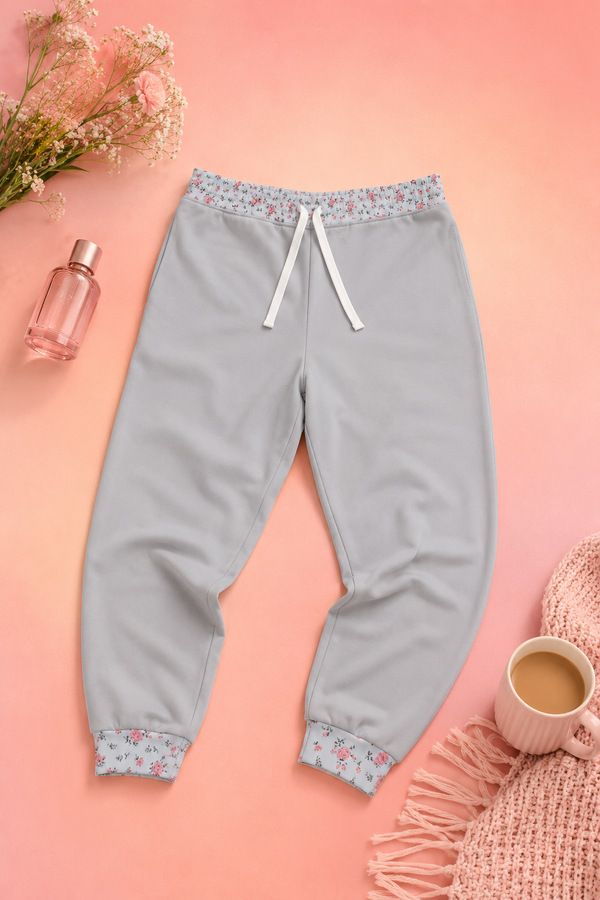 Grey floral joggers styled on a soft pink editorial flat lay background
