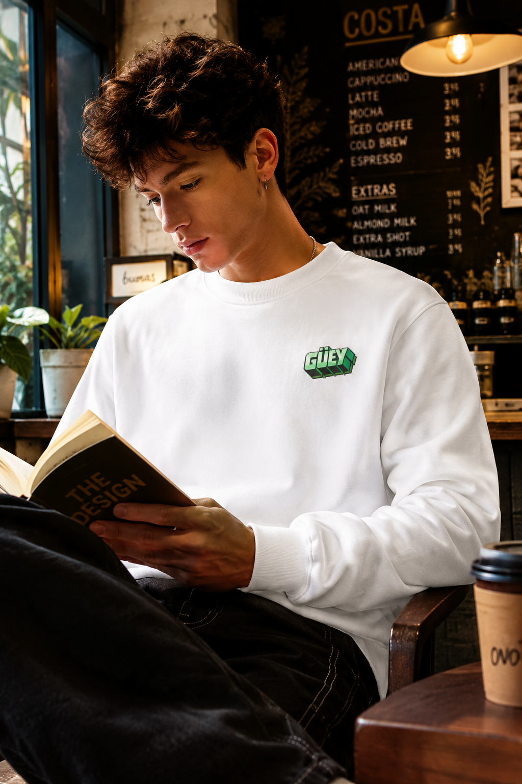 Gen Z man wearing a white Güey Mexican slang sweatshirt while reading in a coffee shop