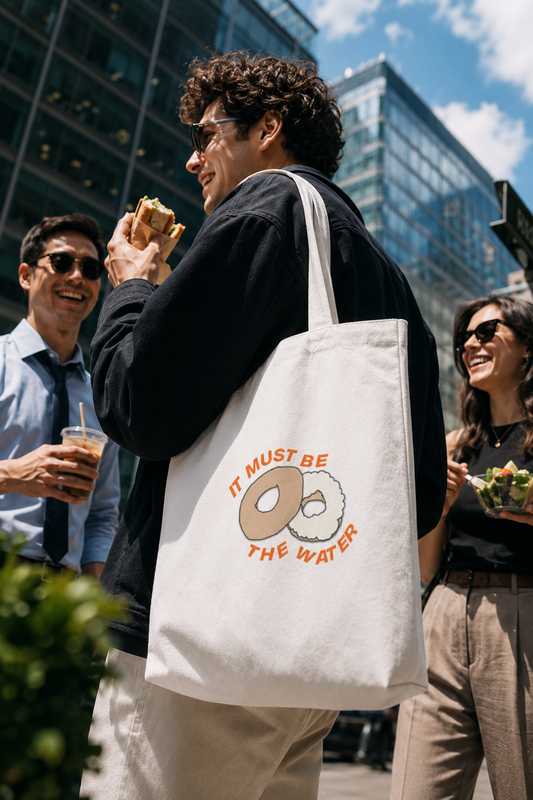 Man carrying a hand-drawn NYC bagel tote bag during a lunch break in Midtown Manhattan.
