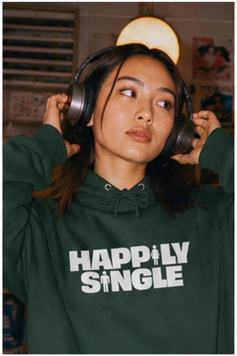 Gen Z woman wearing dark green Happily Single hoodie with headphones in record shop