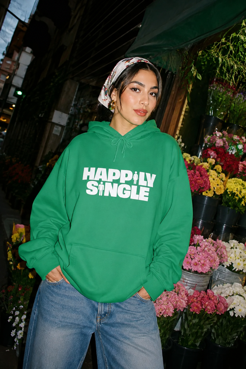 Gen Z woman wearing green Happily Single hoodie outside colorful flower shop