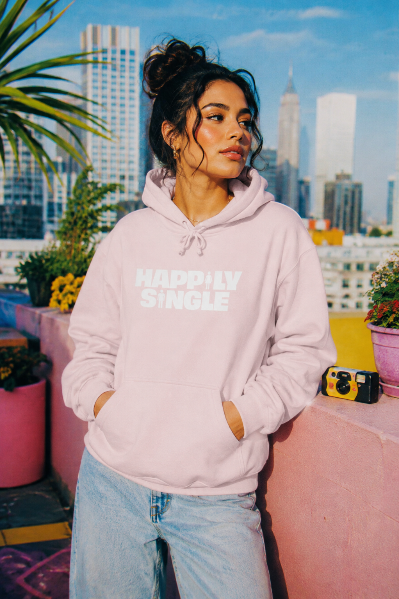 Gen Z woman wearing light pink Happily Single hoodie on colorful city rooftop