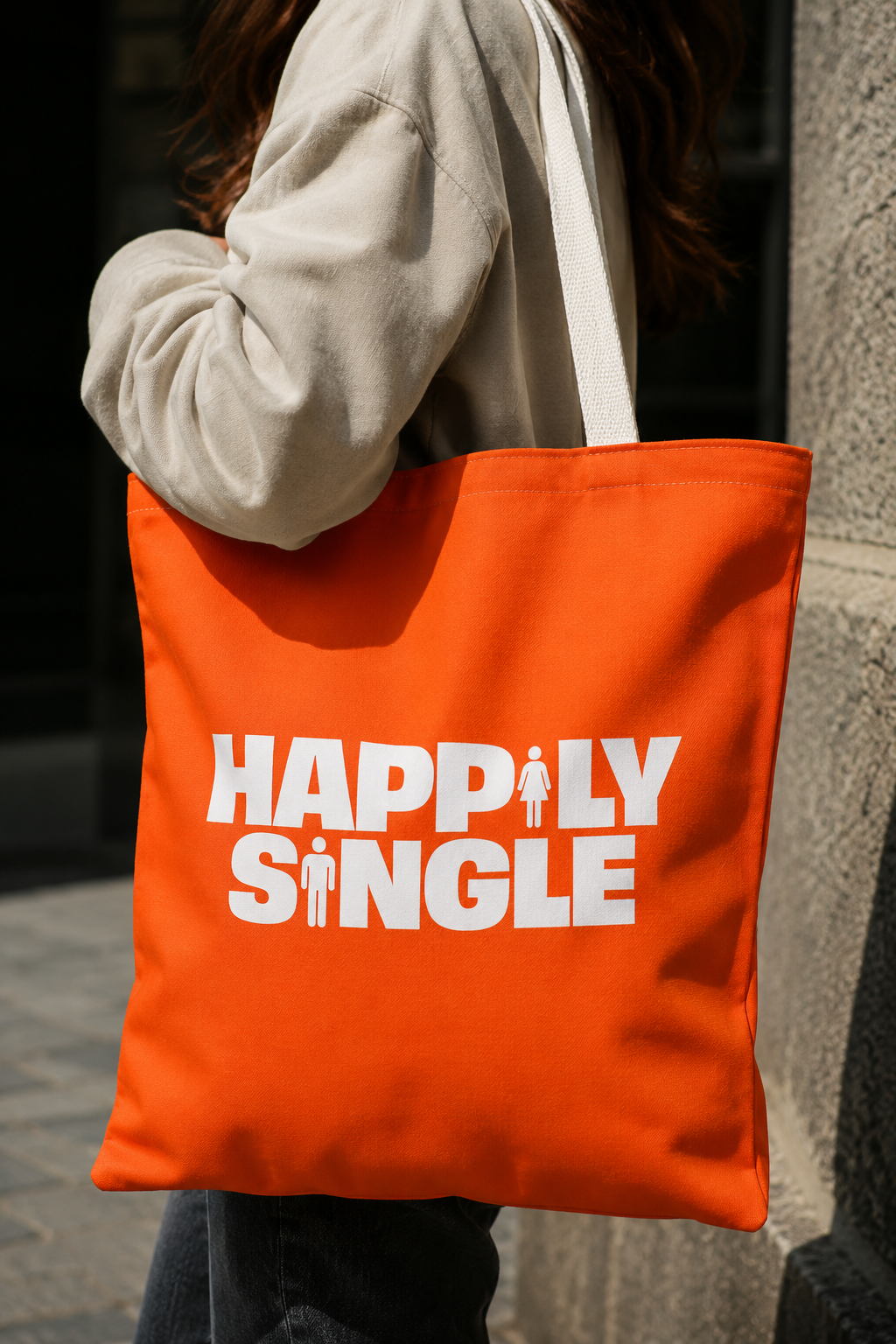 Close-up lifestyle view of an orange Happily Single tote bag with white shoulder straps and bold white graphic.