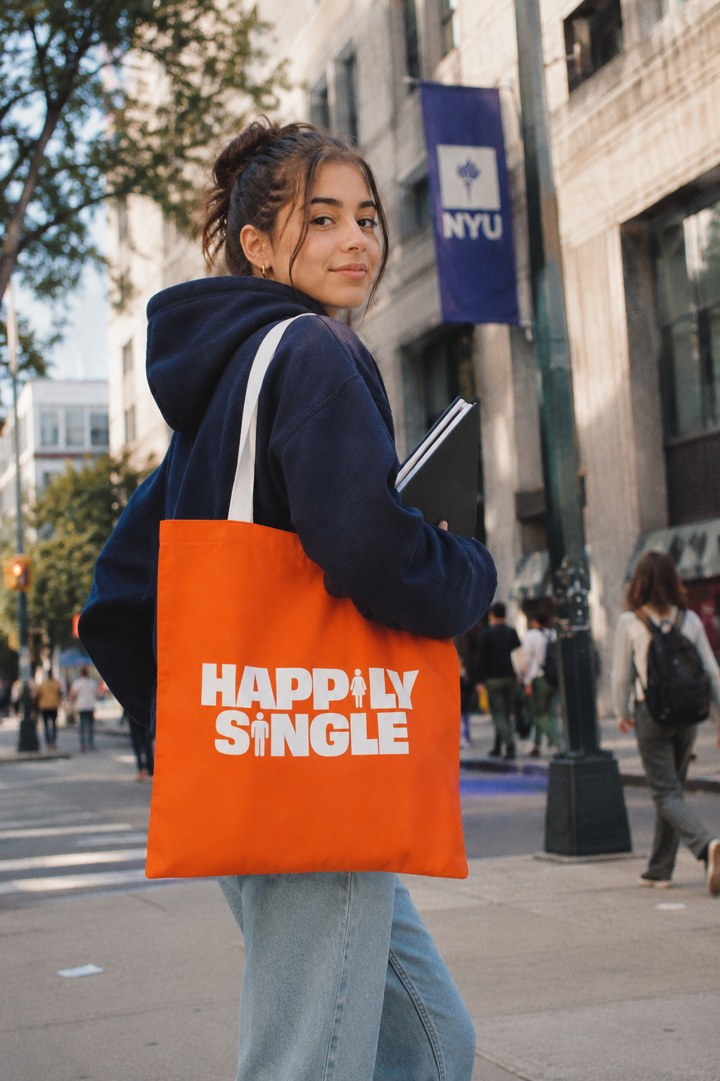 Gen Z college student carrying an orange Happily Single tote bag while walking to class on a city campus.