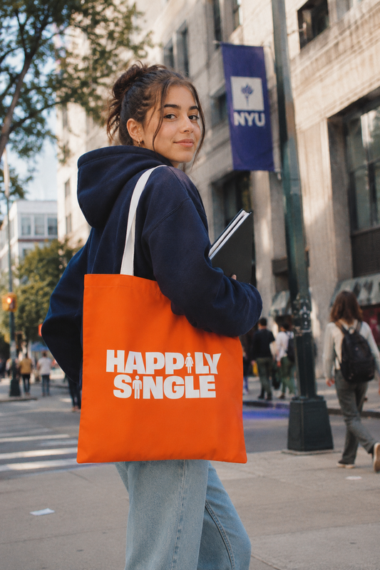 Gen Z college student carrying an orange Happily Single tote bag while walking to class on a city campus.
