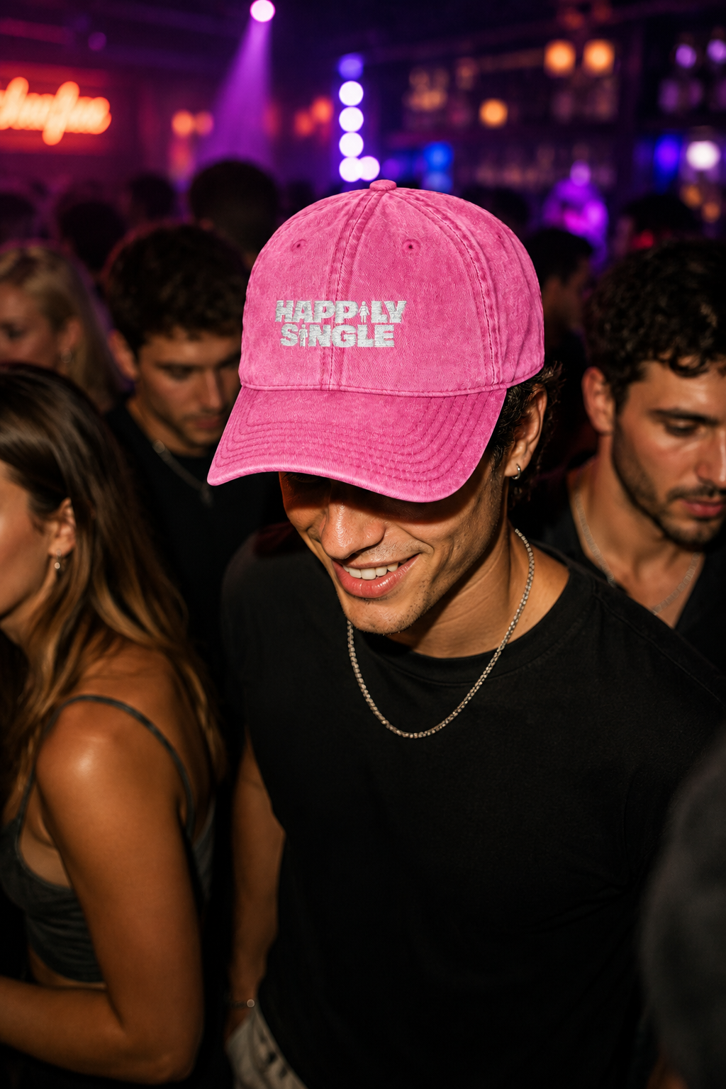 Young man wearing a pink Happily Single baseball cap walking through a crowded nightclub.