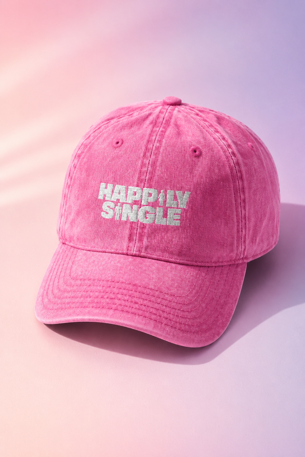Pink Happily Single baseball cap displayed on a soft pastel gradient background.